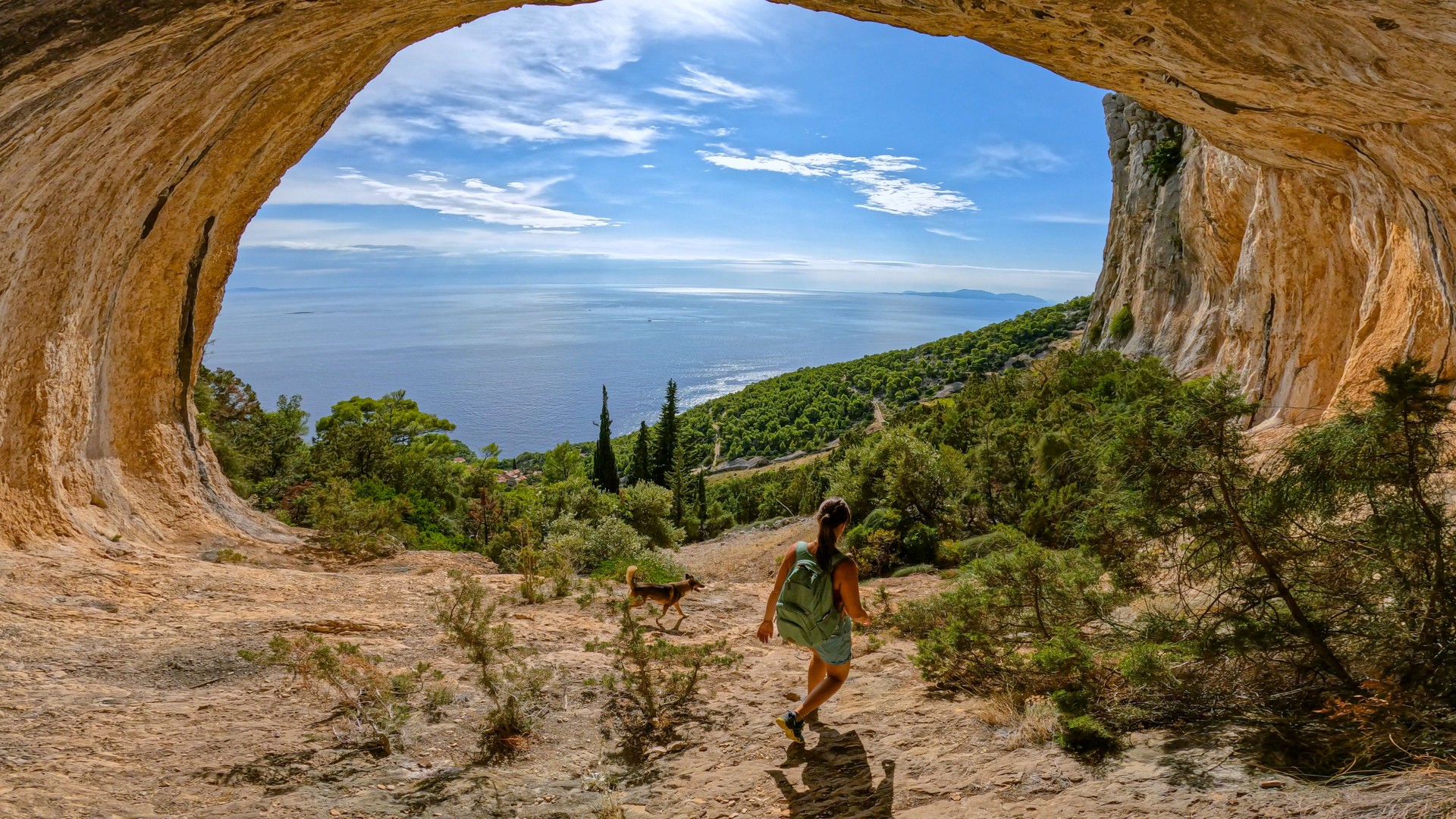Young lady hiking with her dog through scenic mountain hollow with a view of sea